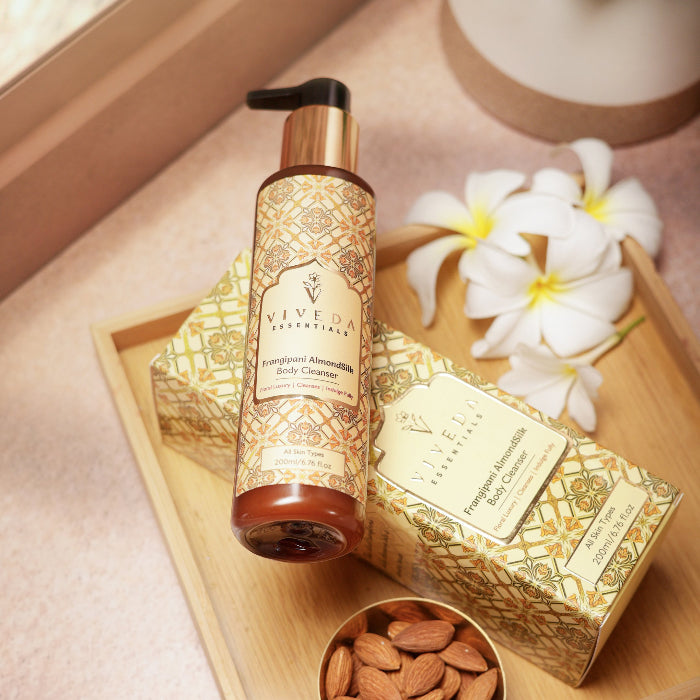 Viveda Frangipani Almondsilk Body Cleanser  bottle and packaging on a wooden tray with flowers and almonds.